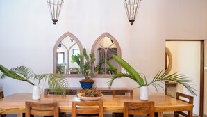 A dining area with a wooden table, six chairs, and two large arched mirrors on the wall.