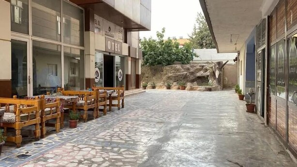 A courtyard with outdoor seating, a stone floor, and a building with a sign that reads "OETI". - Hotel El Muhtar (Akcakale)