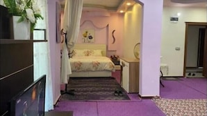 A bedroom with a bed, a nightstand, a mirror, and a door leading to another room. - Hotel El Muhtar (Akcakale)