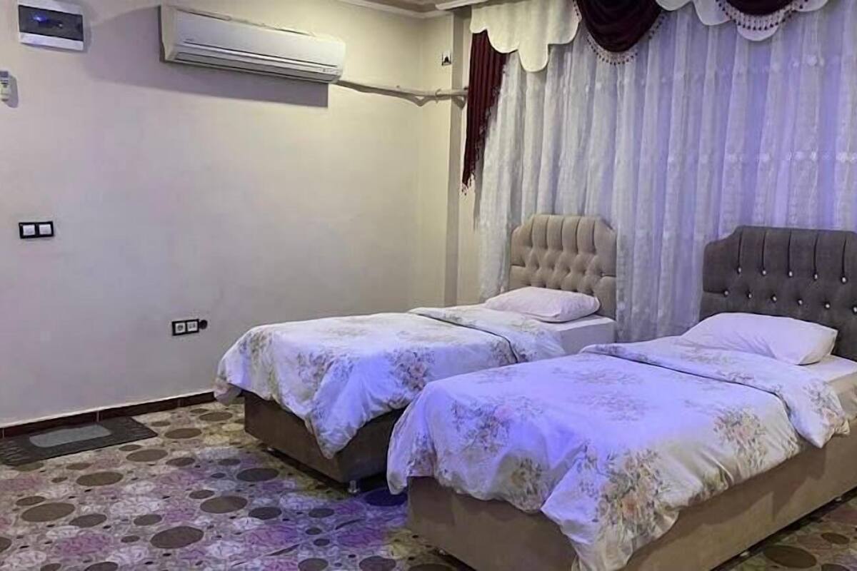 A bedroom with two beds, an air conditioning unit, and a patterned floor.