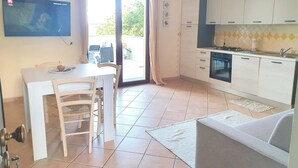 A compact kitchen with a dining area, a sofa, and a TV on the wall. - Bilocale Confort Viviana-LaCiaccia Style (La Ciaccia)