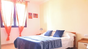 A bedroom with a bed, curtains, a nightstand, and a wall with two pictures. - Bilocale Confort Viviana-LaCiaccia Style (La Ciaccia)