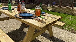 A wooden picnic table set outdoors with plates, cutlery, and drinks.