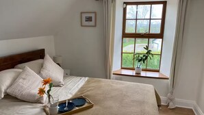A neatly made bed with pillows, a tray with a glass and plate, and a window with a plant.