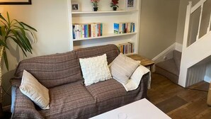 A cozy living room with a brown sofa, two pillows, a white coffee table, and a bookshelf filled with books and decorative items.