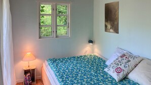 Et soveværelse med seng, et vindue, en sengetavlelampe og en lampe monteret på væggen.