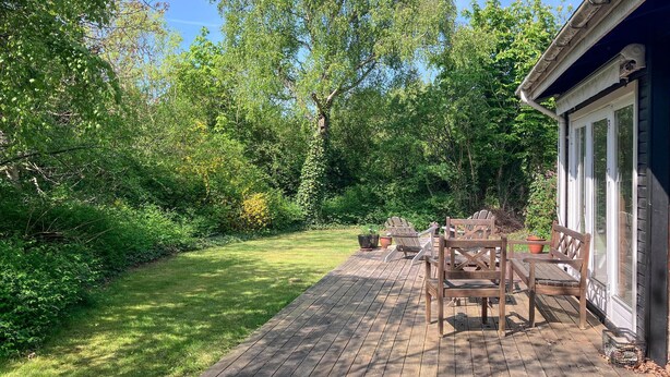 A wooden deck with outdoor furniture, surrounded by lush greenery and trees. - 2 bedroom beautiful home in Jægerspris (Jægerspris)
