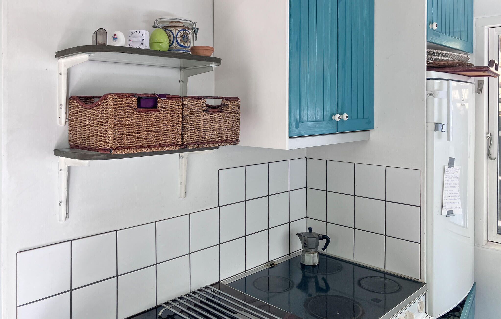 A kitchen with white tiled walls, a stove, and two wicker baskets on a shelf.