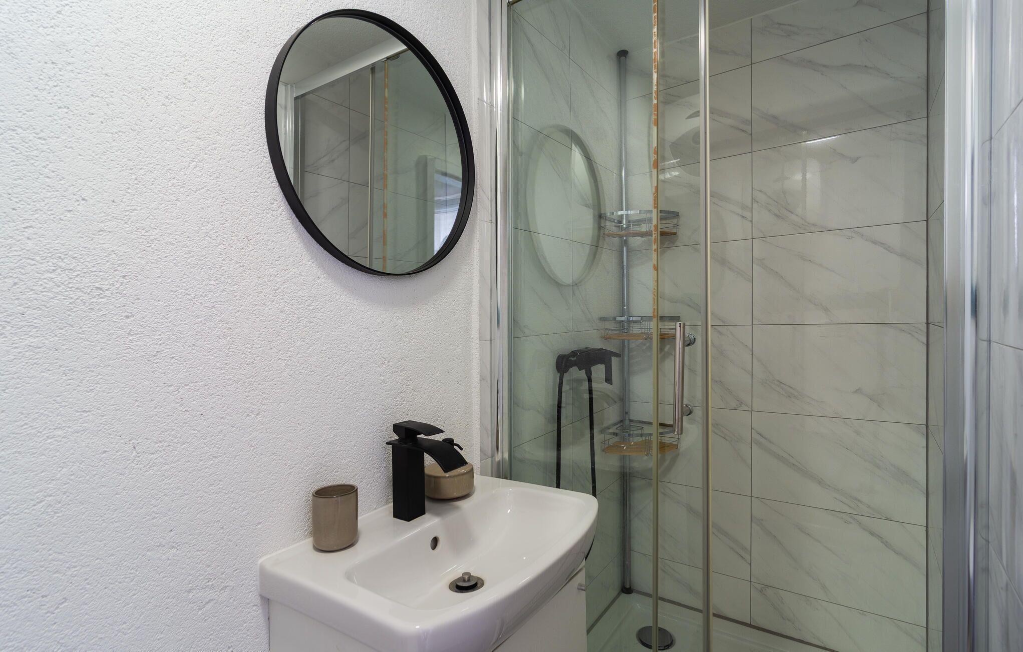 A bathroom with a white sink, a round mirror, and a glass shower enclosure.