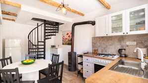 A compact kitchen with a central island, a built-in stove, and a spiral staircase leading to an upper level. - Cozy home in Podosoje (Podosoje)