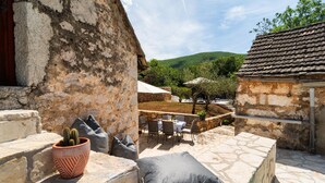 A stone patio with outdoor seating, a cactus in a pot, and a view of a green hillside. - Cozy home in Podosoje (Podosoje)