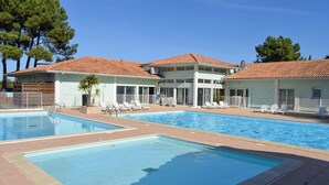 A pool area with two separate swimming pools, lounge chairs, and a building with a tiled roof. - Awesome home in Dolus-d'Oléron with sauna (Dolus-d'Oléron)