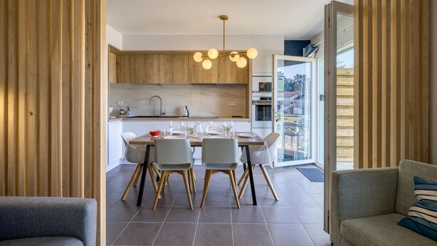 A modern kitchen with wooden cabinets, a marble countertop, and a dining area with a table set for four. - Awesome home in Dolus-d'Oléron with sauna (Dolus-d'Oléron)