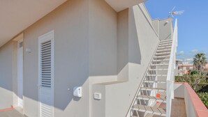 Ein Wohngebäude mit weißer Fassade, einer sichtbaren Tür und einer Treppe, die zu einer oberen Etage führt.