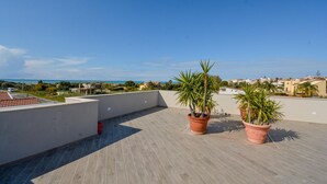 Eine Dachterrasse mit Topfpflanzen, freier Meerblick und eine entfernte Stadtansicht.