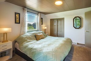 Un dormitorio con cama, lámparas de noche, ventana con cortinas, puerta y espejo montado en la pared.