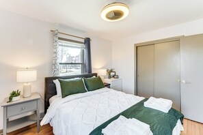 A neatly made bed with a white and green quilt, a bedside lamp, a small plant, and a window with a curtain.