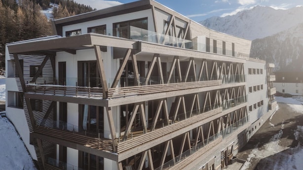 Un edificio moderno con múltiples balcones y amplias ventanas, con montañas al fondo.