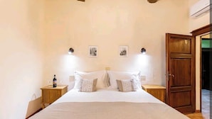 A bedroom with a large bed, two bedside tables, a wooden wardrobe, and two wall-mounted lights. - Casa Gioia - Casa Olivieri  (Pienza)