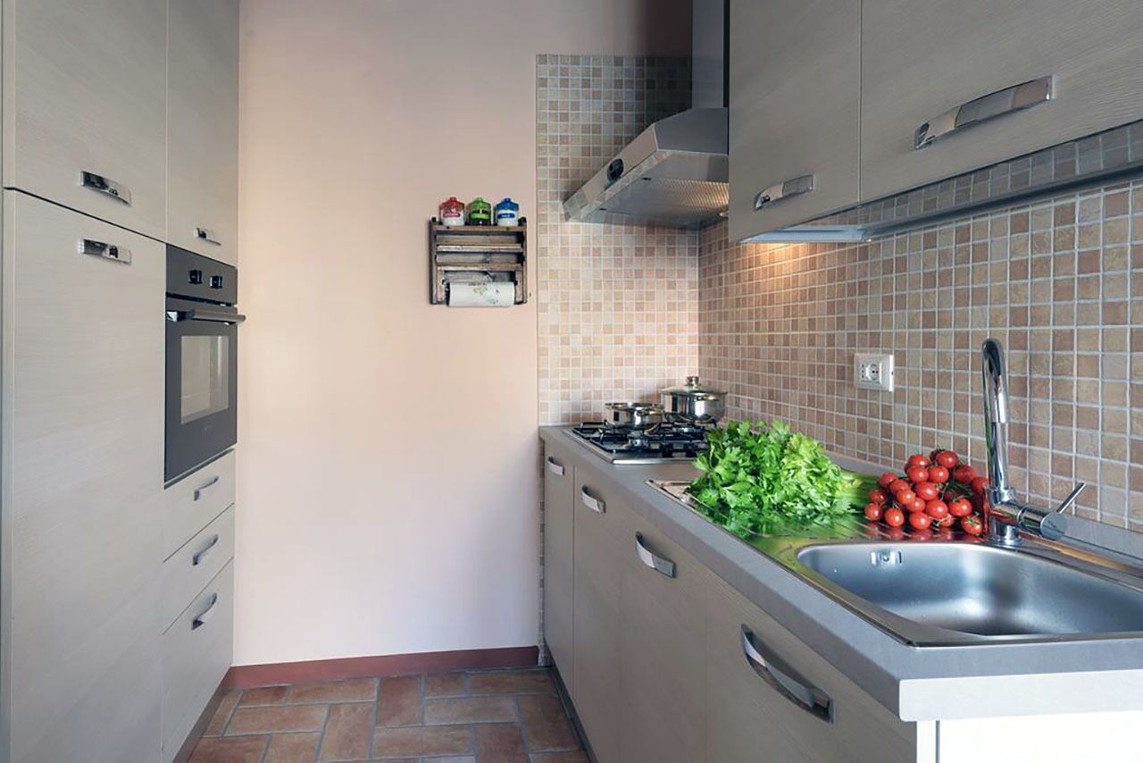 A compact kitchen with a built-in oven, a gas stove, a stainless steel sink, and a tiled backsplash.
