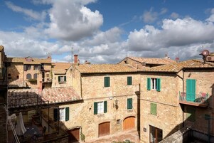 Edificio de piedra tradicional con varias ventanas y puertas, un patio con mesa y sillas, y un cielo azul despejado con nubes.