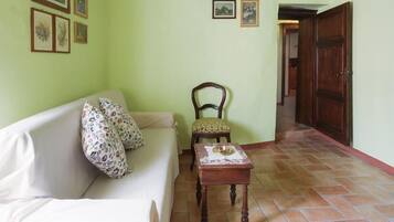 Un salon comprenant un canapé, une chaise en bois, une petite table et une porte donnant sur une autre pièce.