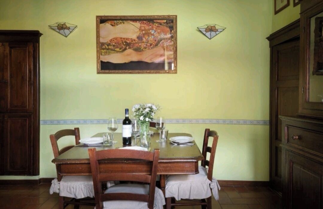 A dining area with a wooden table set for two, a wine bottle, and a vase with flowers.