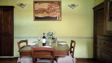 A dining area with a wooden table set for two, a wine bottle, and a vase with flowers.