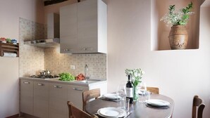 A kitchen with a dining table set for two, a gas stove, and a potted plant on the wall. - Casa Gioia - Casa Olivieri  (Pienza)
