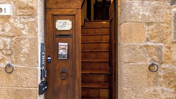 A stone building with a wooden door, a staircase, and a small window with a metal grill. - Casa Gioia - Casa Olivieri  (Pienza)