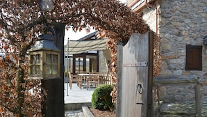 A stone building with a wooden door, a lantern, and a cobblestone path leading to an outdoor seating area. - Farmhouse in Belgium Near Lake Coo & Jacuzzi (Trois-Ponts)