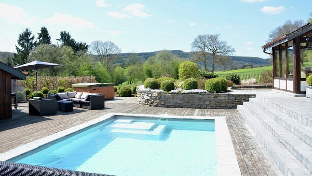 A swimming pool with a wooden deck, outdoor furniture, and a stone wall with topiary. - Farmhouse in Belgium Near Lake Coo & Jacuzzi (Trois-Ponts)