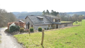 A stone house with a sloped roof, a small porch, and a fenced yard. - Farmhouse in Belgium Near Lake Coo & Jacuzzi (Trois-Ponts)