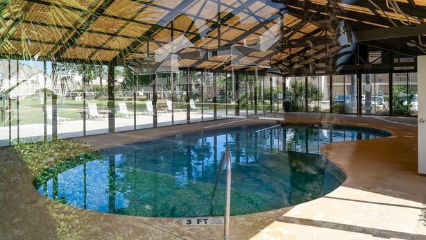 An indoor swimming pool with a glass enclosure, a 3 FT depth marker, and a thatched roof structure. - Bay Tree cozy 2BR condo on the ground floor (Little River)