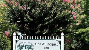 A sign for 'Bay Tree Golf & Racquet and Golf Colony IX' with a white picket fence and a large flowering tree in the background. - Bay Tree cozy 2BR condo on the ground floor (Little River)