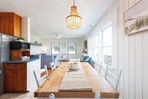 Una cocina luminosa con una mesa de madera, sillas blancas y una araña.