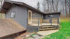 Een modern huis met een houten terras, een klein portaaltje en een betonnen pad naar de deur.