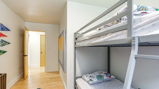 Een slaapkamer met stapelbedden, een houten vloer, een klein krukje en een kleurrijk vloerkleed.