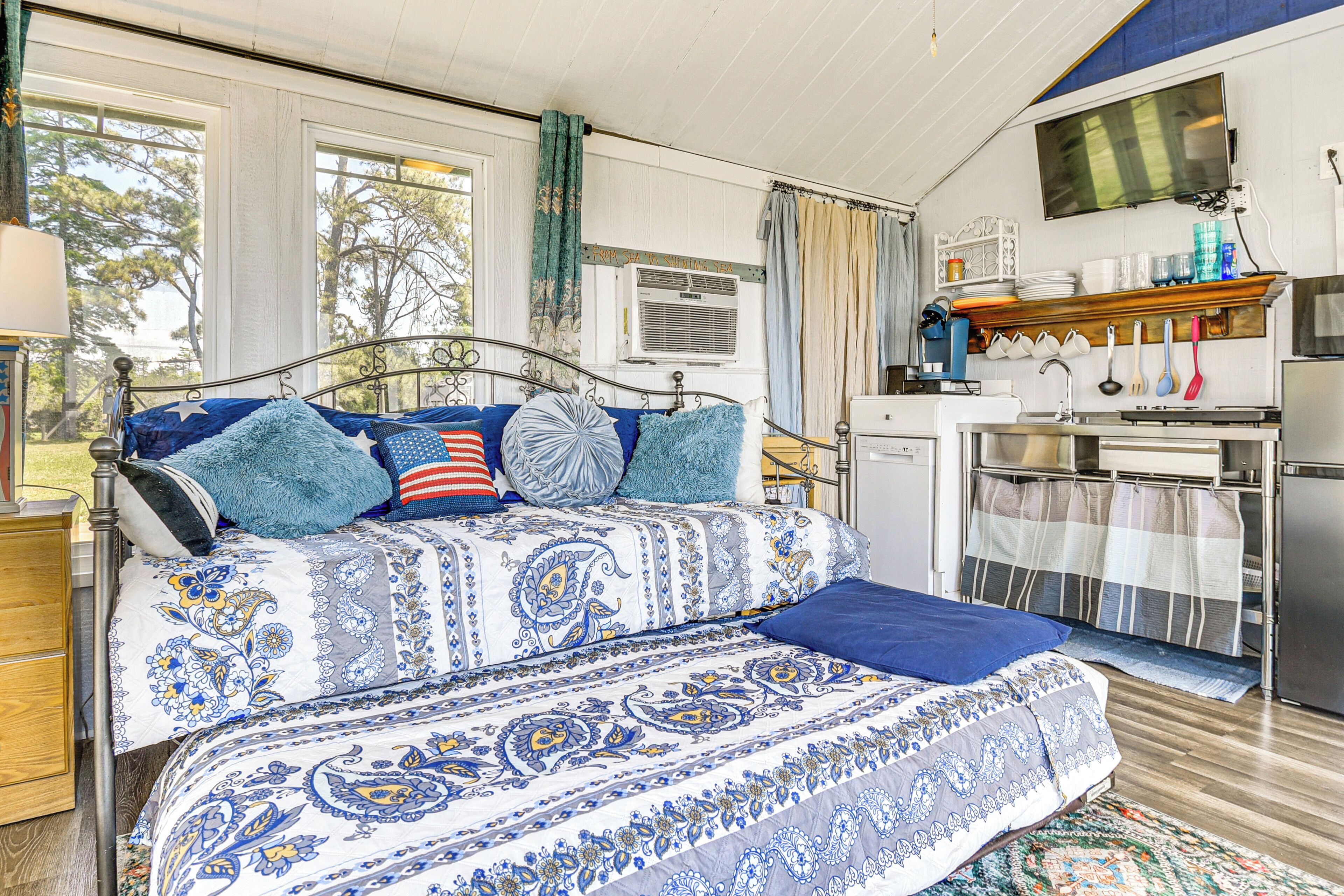 Une chambre avec un lit, un petit coin cuisine et une fenêtre avec des rideaux.
