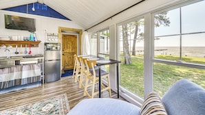 A compact kitchen with modern appliances, a dining area with wooden chairs, and large windows offering a view of the beach. - Tiny House w/ Big Views: Cabin in Shiloh! (Shiloh)