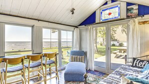 A room with a large sliding glass door leading to a patio, a bed with a 'Hello' pillow, wooden chairs, and a patterned rug. - Tiny House w/ Big Views: Cabin in Shiloh! (Shiloh)