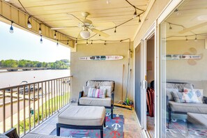 Ein Balkon mit Deckenventilator, zwei gepolsterte Stühle, einem Surfbrett und Blick auf einen Fluss.