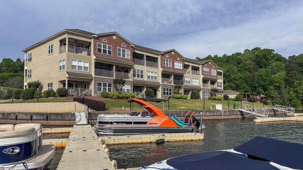 Un immeuble résidentiel à plusieurs étages doté de balcons, un quai avec des bateaux, et un pont en arrière-plan.