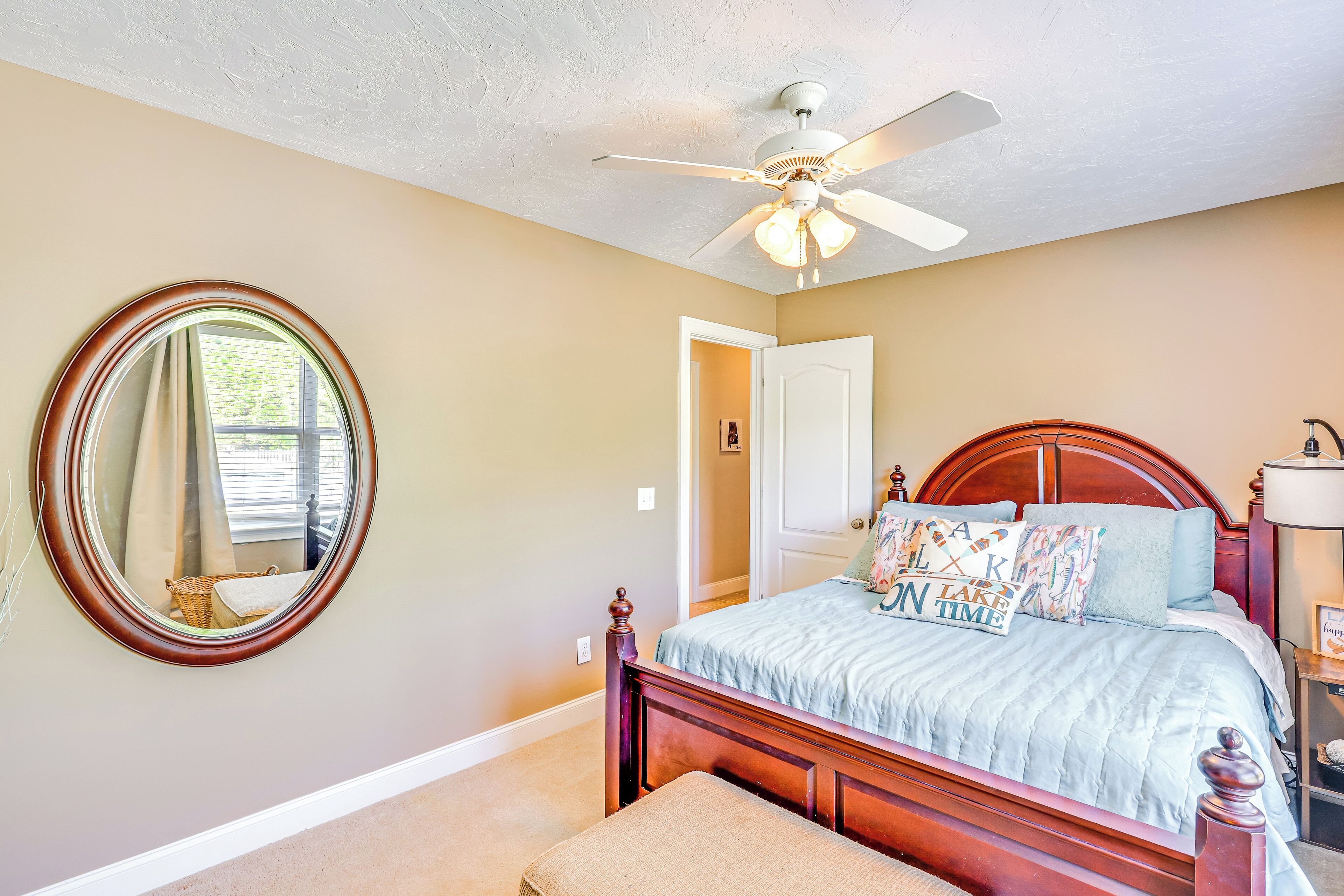 A bedroom with a wooden bed, a round mirror, a ceiling fan, and a door leading to another room.