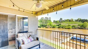 Un balcon avec un canapé, une porte vitrée et une vue sur une rivière où naviguent des bateaux.
