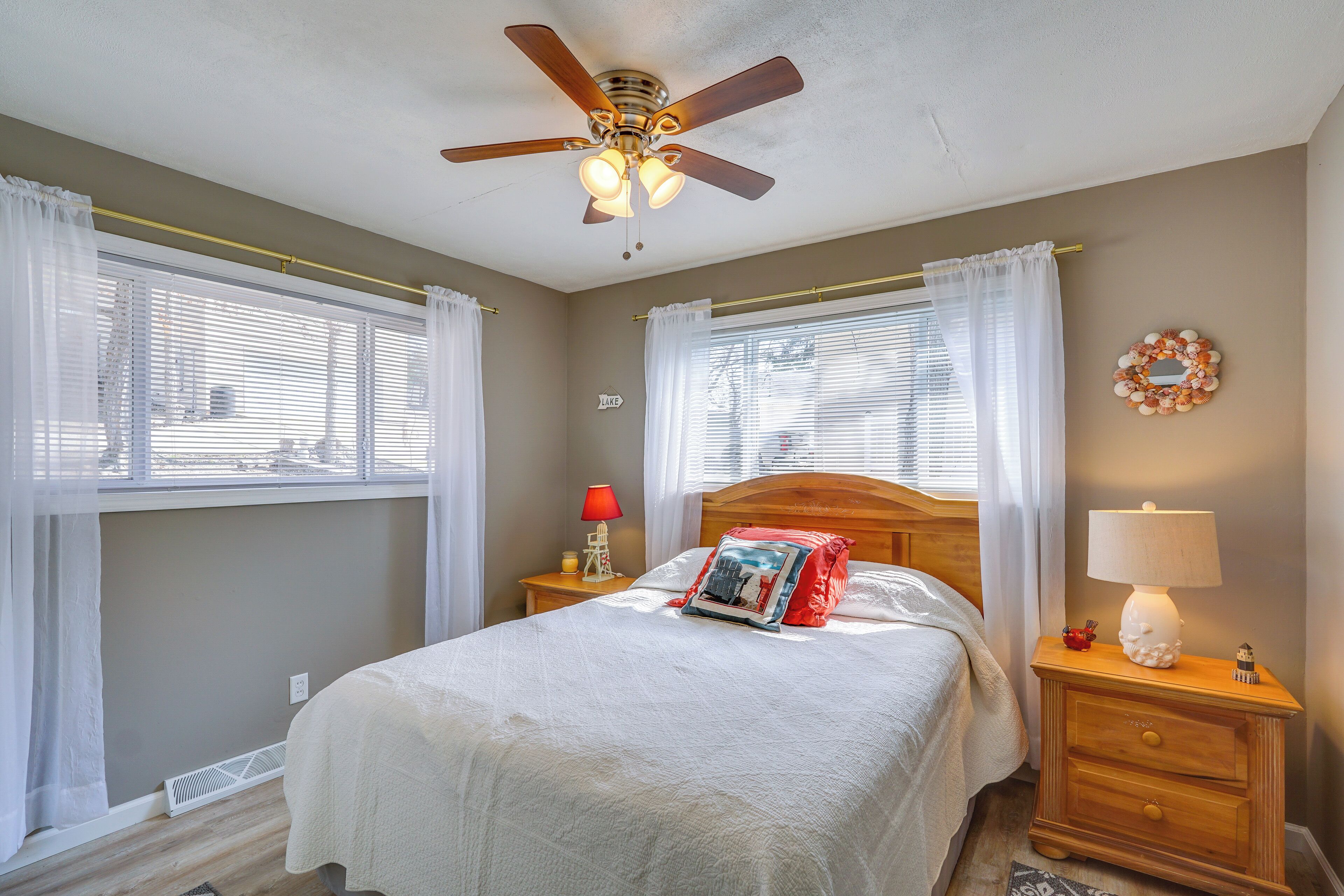 A bedroom with a bed, a nightstand with a lamp, a ceiling fan, and a window with curtains.