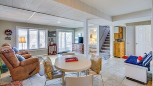 A spacious living area with a large round table, comfortable seating, a staircase, and a view of the outdoors.