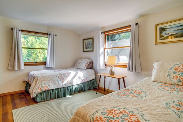 A bedroom with two beds, a nightstand, a window with curtains, and a painting on the wall.