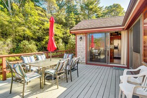 A deck with a glass door leading to a kitchen, surrounded by a wooden deck and a red umbrella.