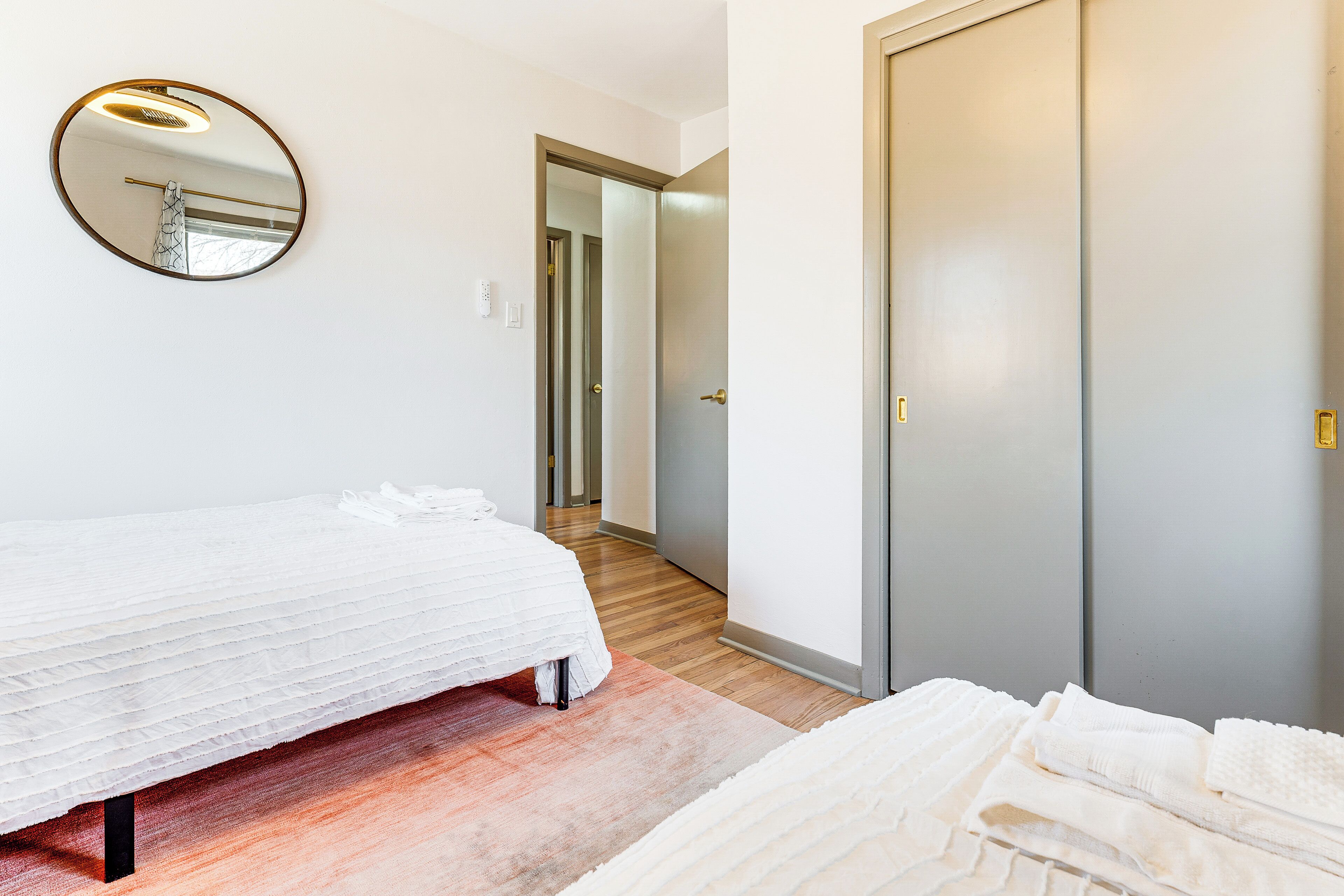 A bedroom with a bed, a round mirror, a wardrobe, and a hallway leading to another room.